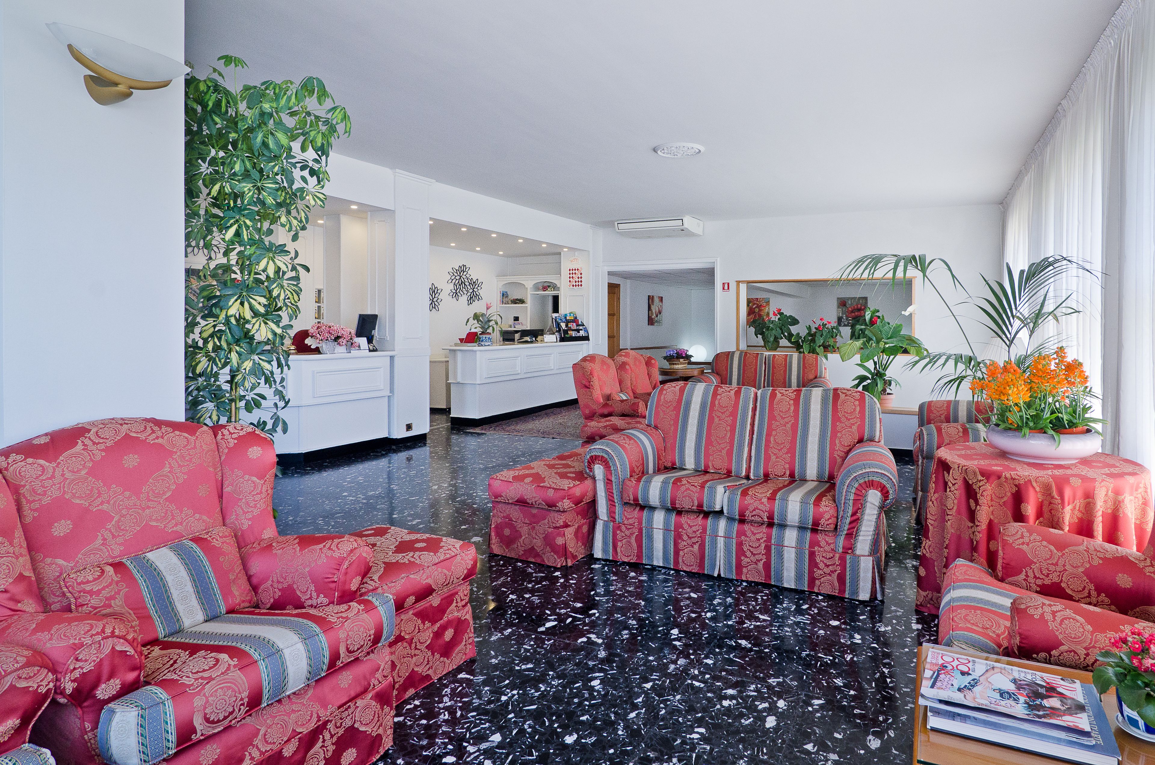 A spacious living room with a black marble floor, red patterned sofas, and a large potted plant.
