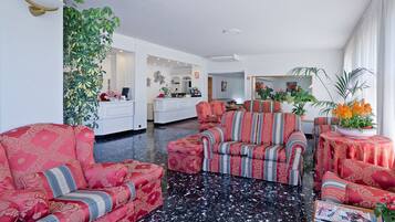 A spacious living room with a black marble floor, red patterned sofas, and a large potted plant.