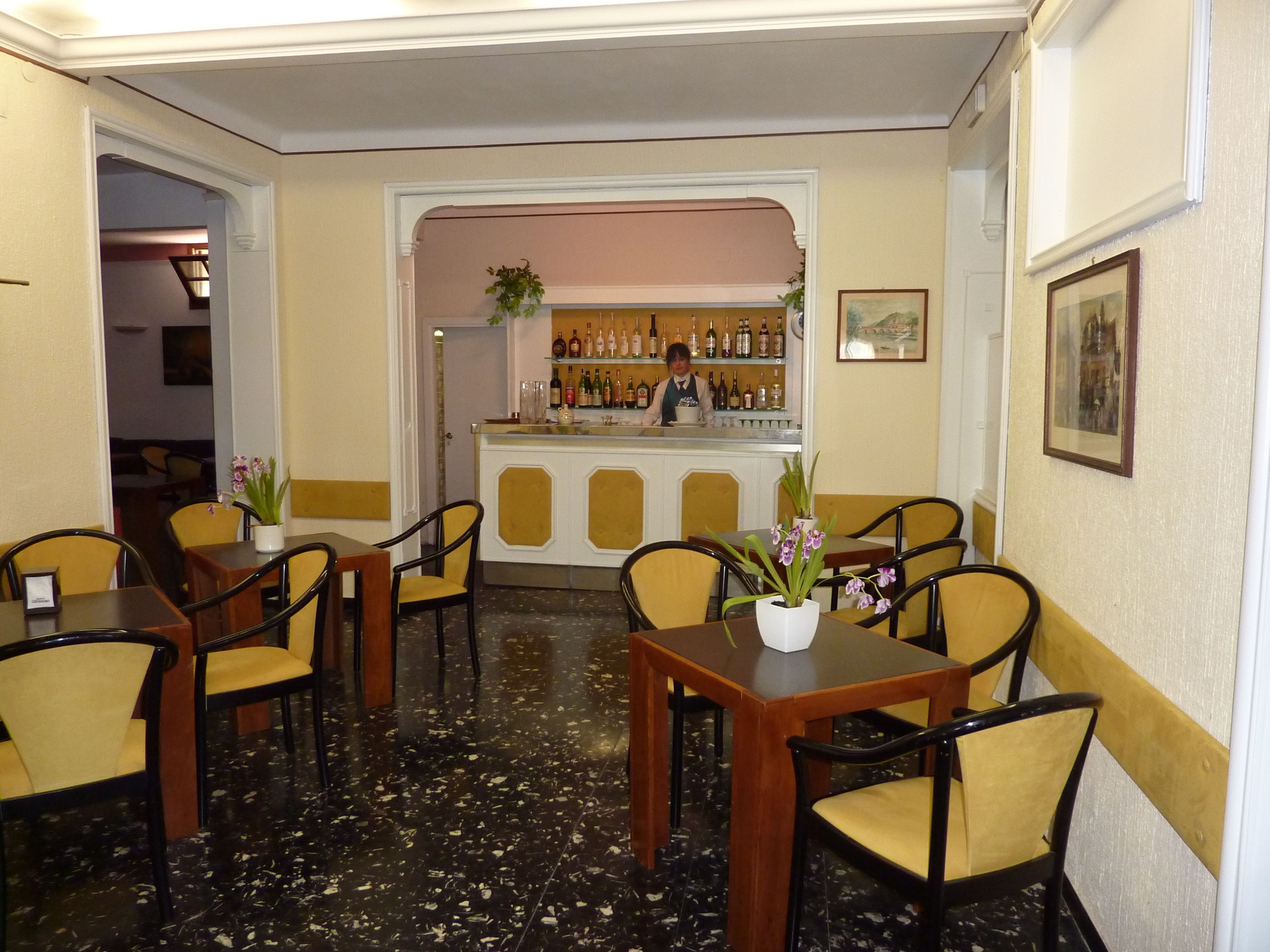 A bar area with a counter, bar stools, and a bartender. There are tables and chairs arranged for dining.