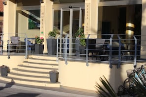 A hotel entrance with a glass door, outdoor seating, and potted plants. - Villa Igea (Diano Marina)