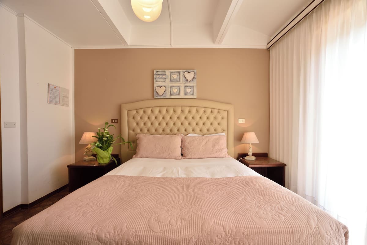 Une chambre d’hôtel avec un grand lit, deux tables de chevet, un luminaire fixé au mur et un ventilateur de plafond.