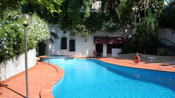 Relax by the serene pool surrounded by lush greenery and a shaded deck.