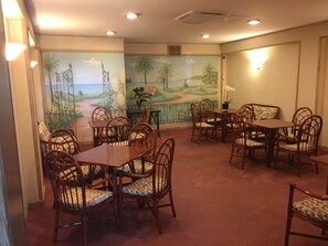 A dining area with wooden tables and chairs, a mural with a landscape scene, and a small table with a vase of flowers. - Hotel Bobby Executive (Sanremo)