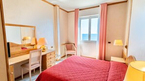 Una habitación de hotel con una cama, un escritorio, una silla, una ventana con cortinas y vistas al mar.