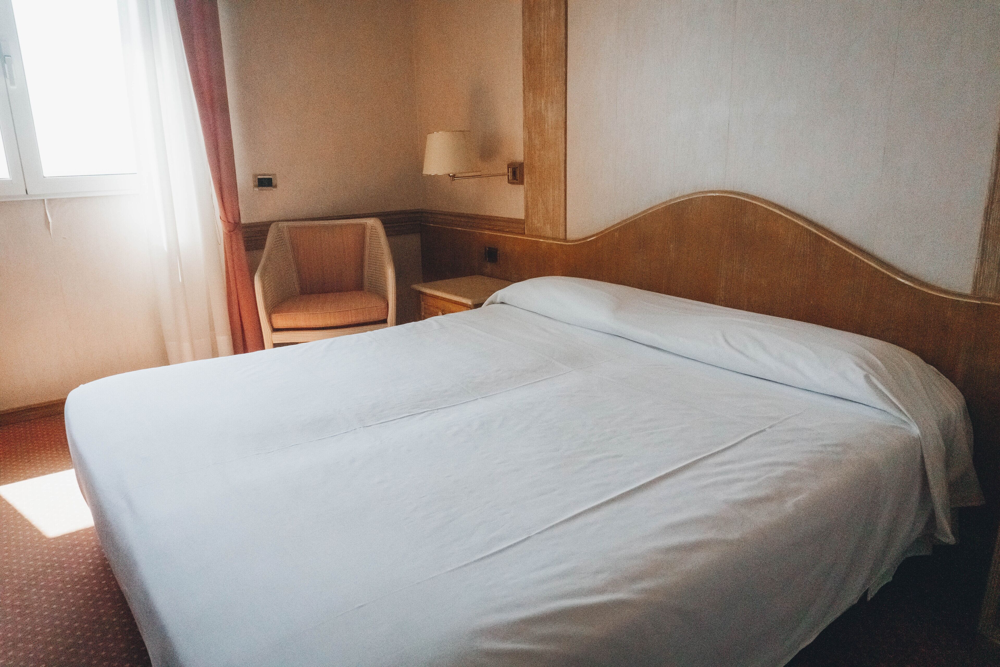 Una habitación de hotel con una cama individual, una silla, una mesita de noche y una lámpara.