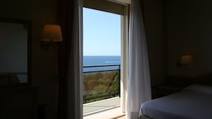 Habitación de hotel con una cama, una mesita de noche, una lámpara y vista al mar a través de una ventana.