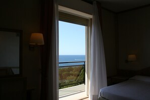 A hotel room with a bed, a nightstand, a lamp, and a view of the sea through a window. - Hotel Bobby Executive (Sanremo)