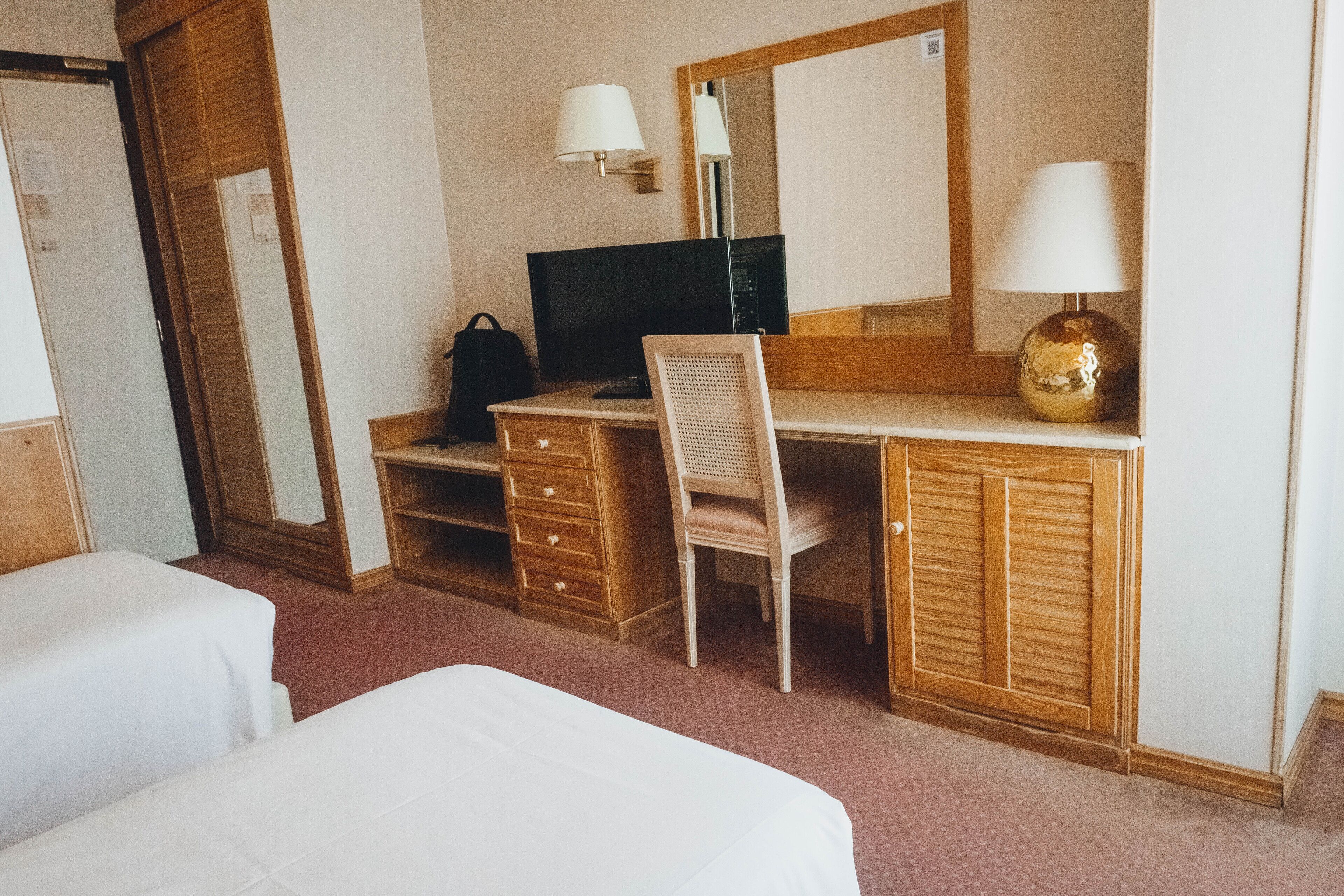 Habitación de hotel con un escritorio de madera, una silla, un televisor, una lámpara y dos camas.