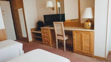 Habitación de hotel con un escritorio de madera, una silla, un televisor, una lámpara y dos camas.