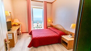 A hotel room with a bed, a desk with a lamp, a chair, and a view of the sea through a balcony. - Hotel Bobby Executive (Sanremo)
