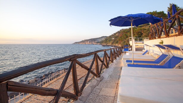 A coastal walkway with a wooden railing, beach umbrellas, and lounge chairs. - Piccolo Paradiso (Massa Lubrense)