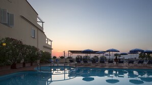 A pool area with lounge chairs and umbrellas, a clear sky, and a building with a balcony. - Piccolo Paradiso (Massa Lubrense)