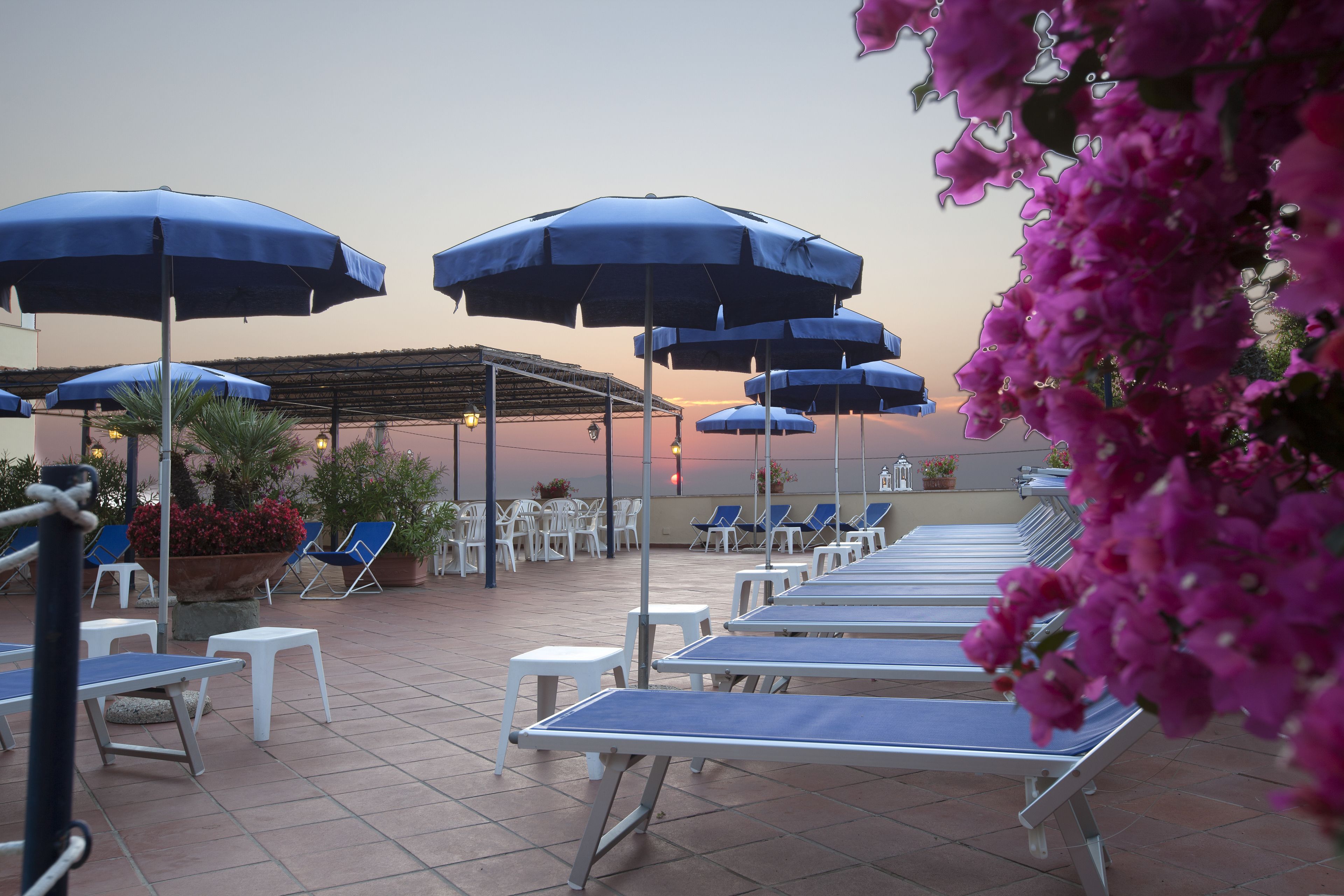 Un espace de détente sur le toit, agrémenté de parasols bleus, de chaises longues blanches et d’un coin salon abrité.