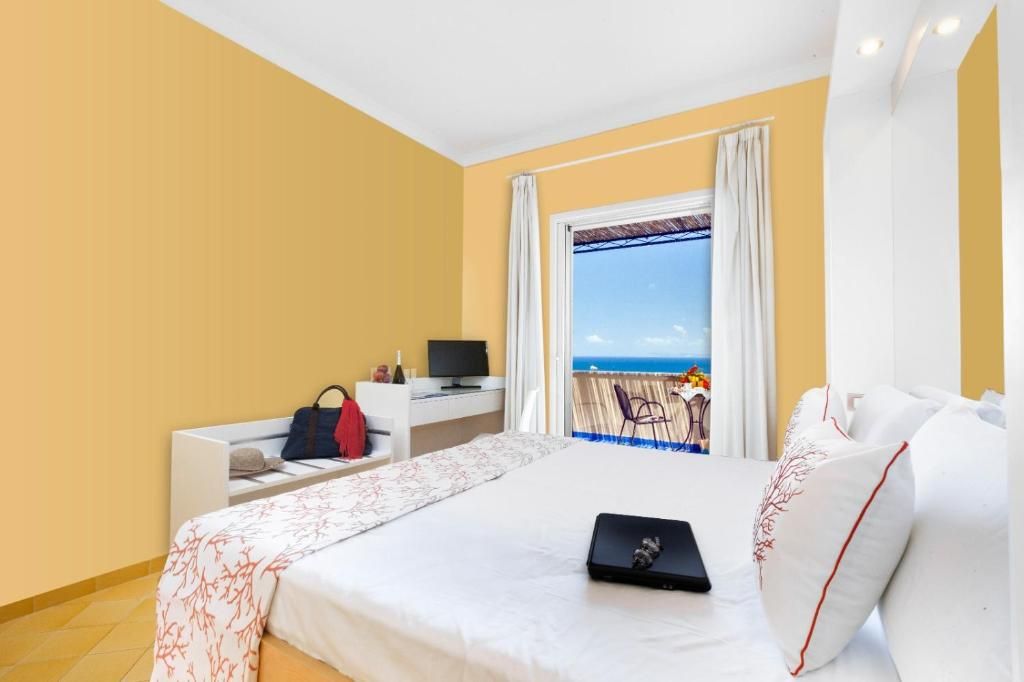 Ein Hotelzimmer mit einem Bett, einem Schreibtisch mit Computer, einem Sessel und Blick auf das Meer.