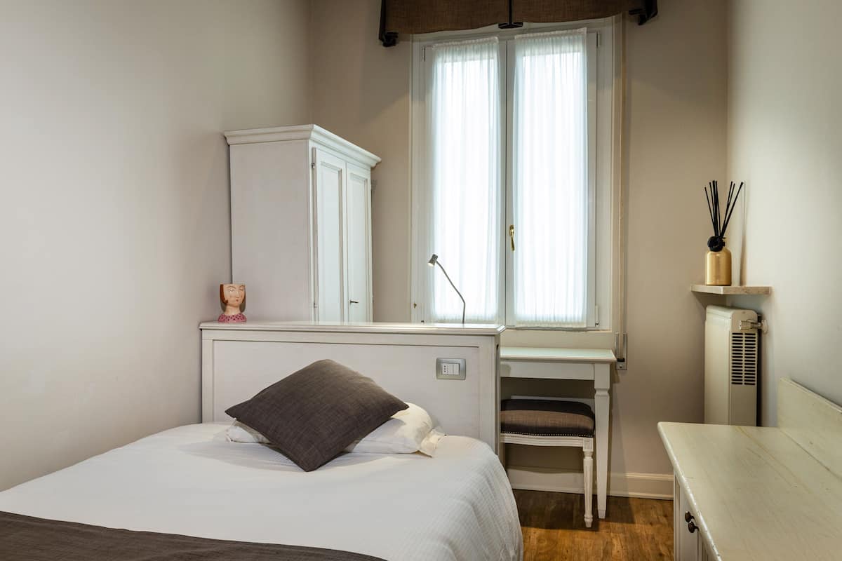 A bedroom with a bed, a desk, a chair, a wardrobe, and a radiator.