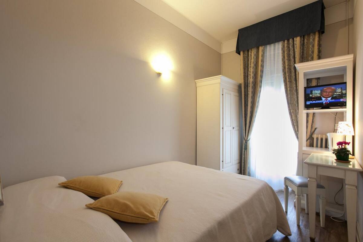 A hotel room with a bed, a desk, a television, and a wardrobe.