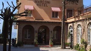 A building with the sign "Marconi Hotel" and red and white striped awnings. There are potted plants and a clear sky. - Hotel Marconi (Sirmione)