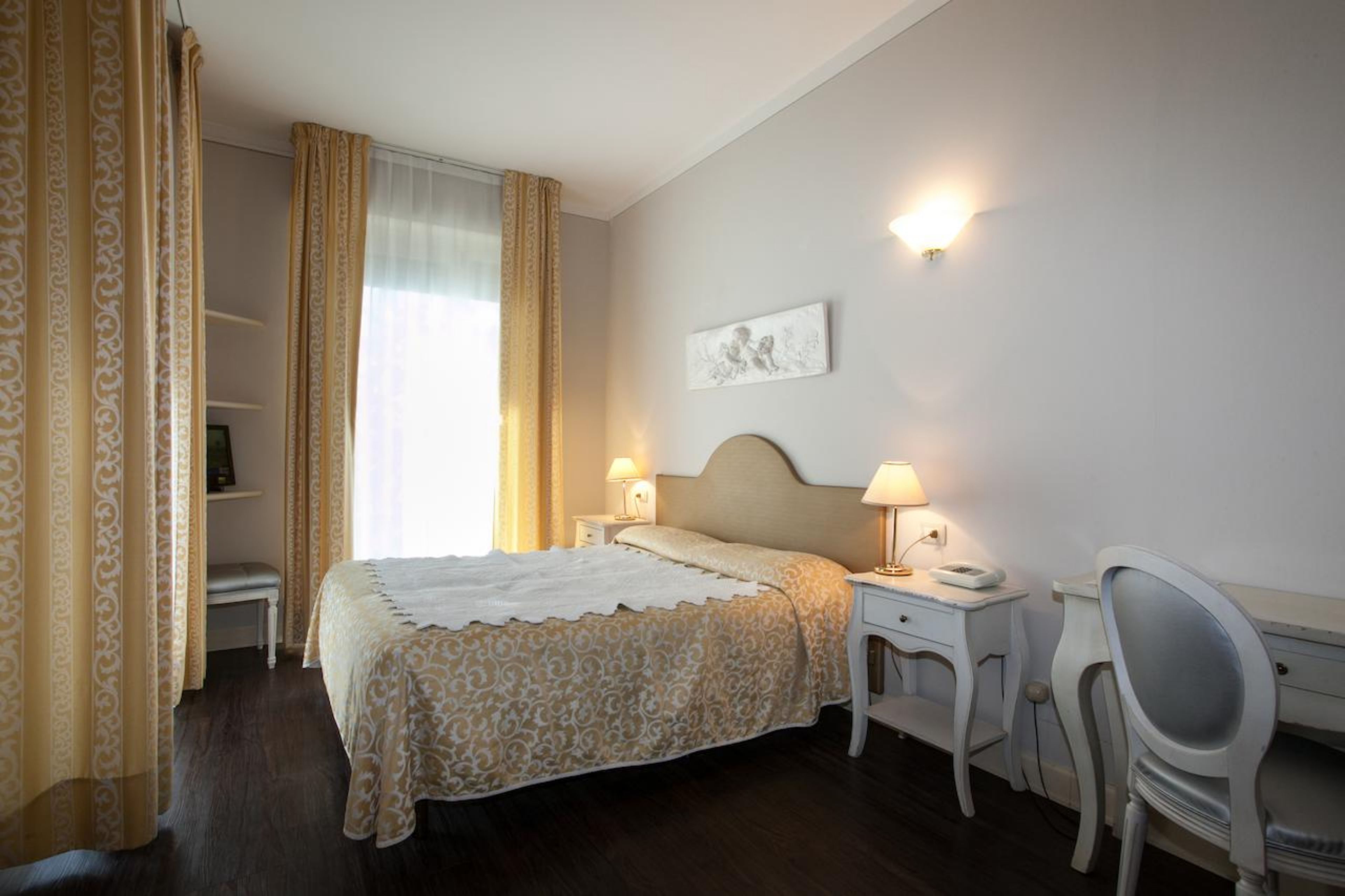 A hotel room with a bed, bedside tables, a desk, and a chair.