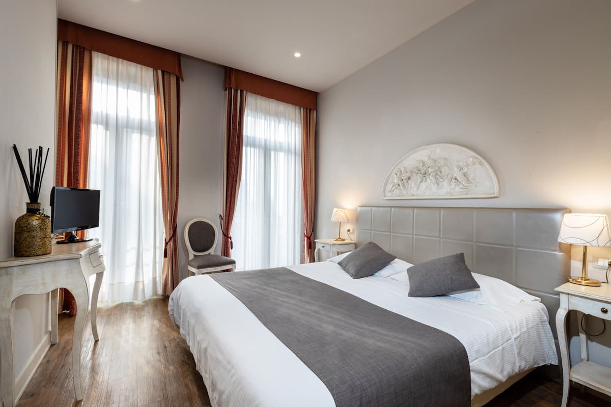 A hotel room with a large bed, a desk with a computer, a chair, and a decorative wall piece.