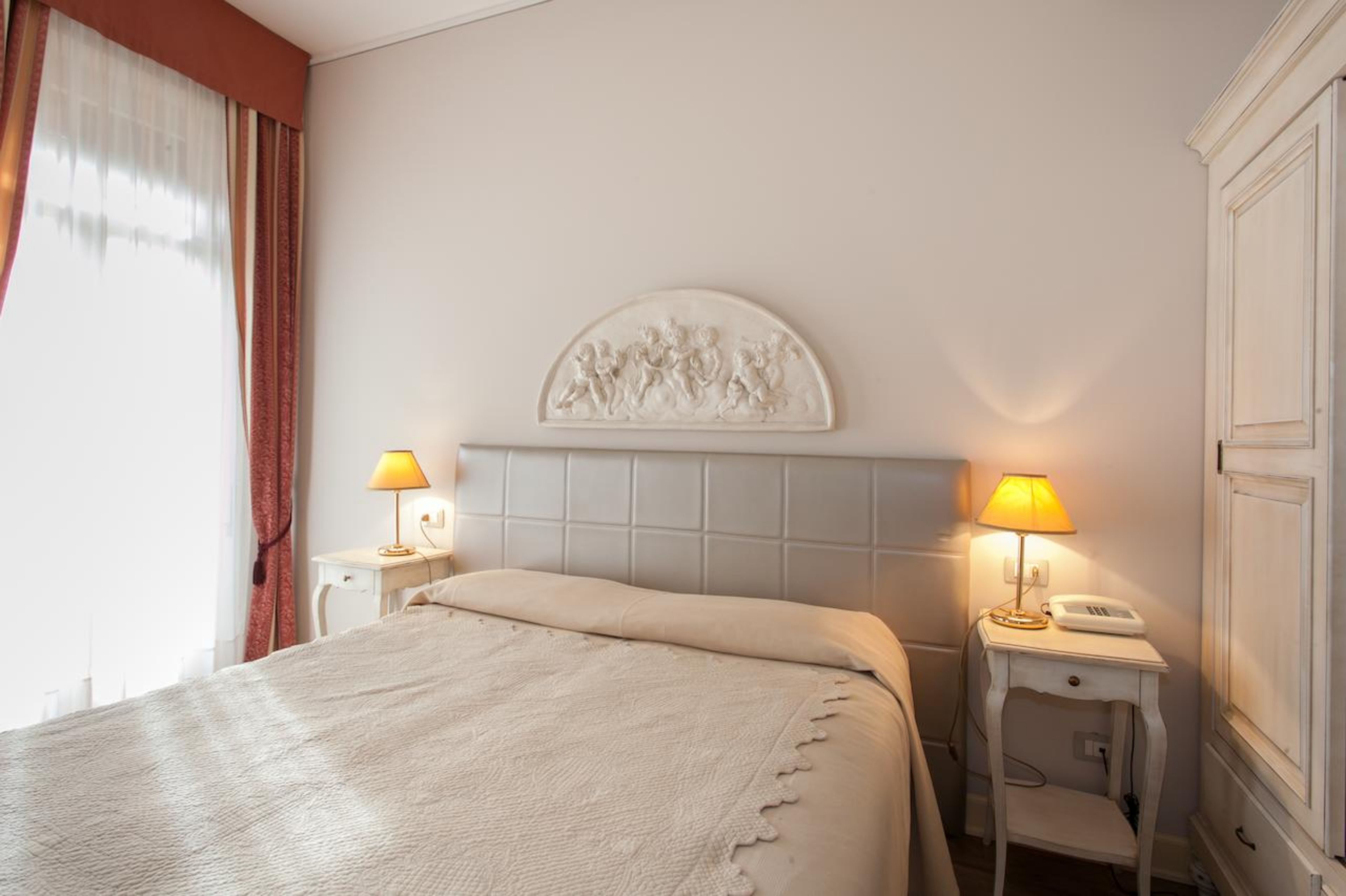 Habitación de hotel con una cama grande, dos mesitas de noche con lámparas, un adorno en la pared y un armario.