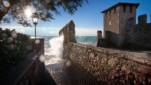 A stone pathway leading to a sea view, flanked by ancient stone walls and a lamp post. - Hotel Marconi (Sirmione)
