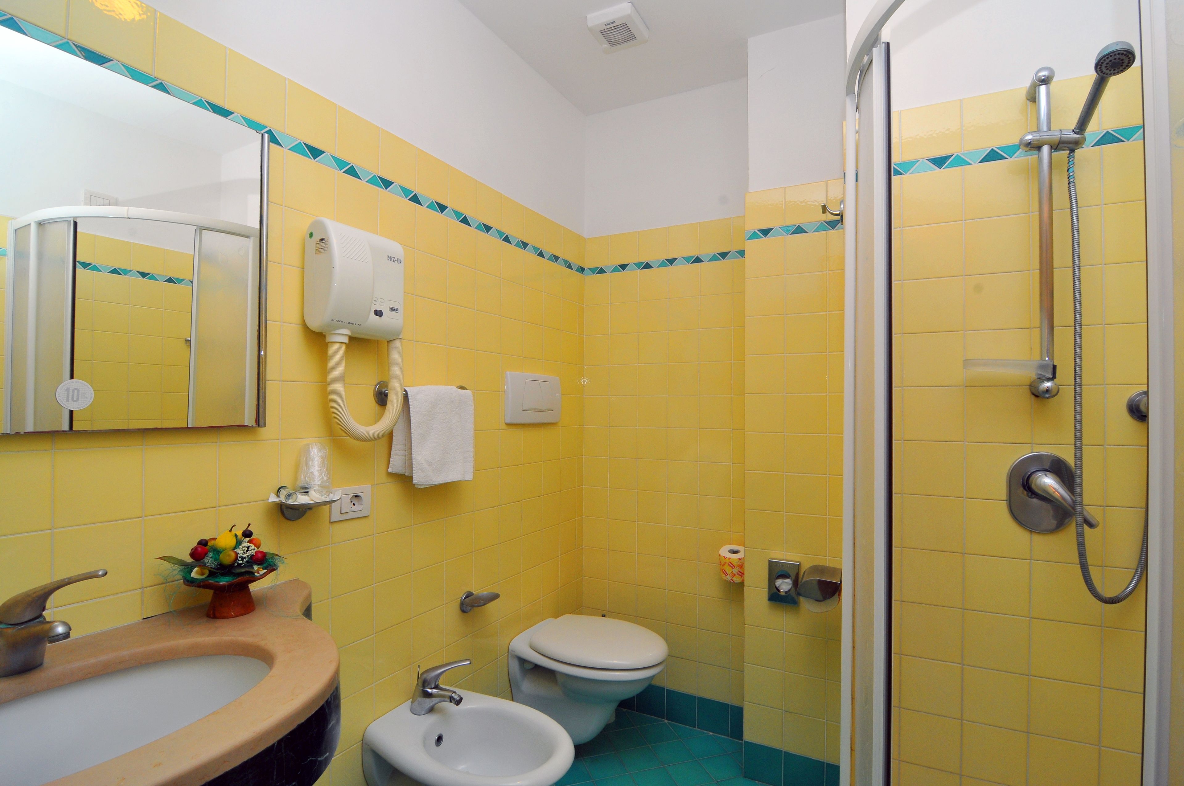 A bathroom with yellow tiles, a sink, a toilet, and a shower.