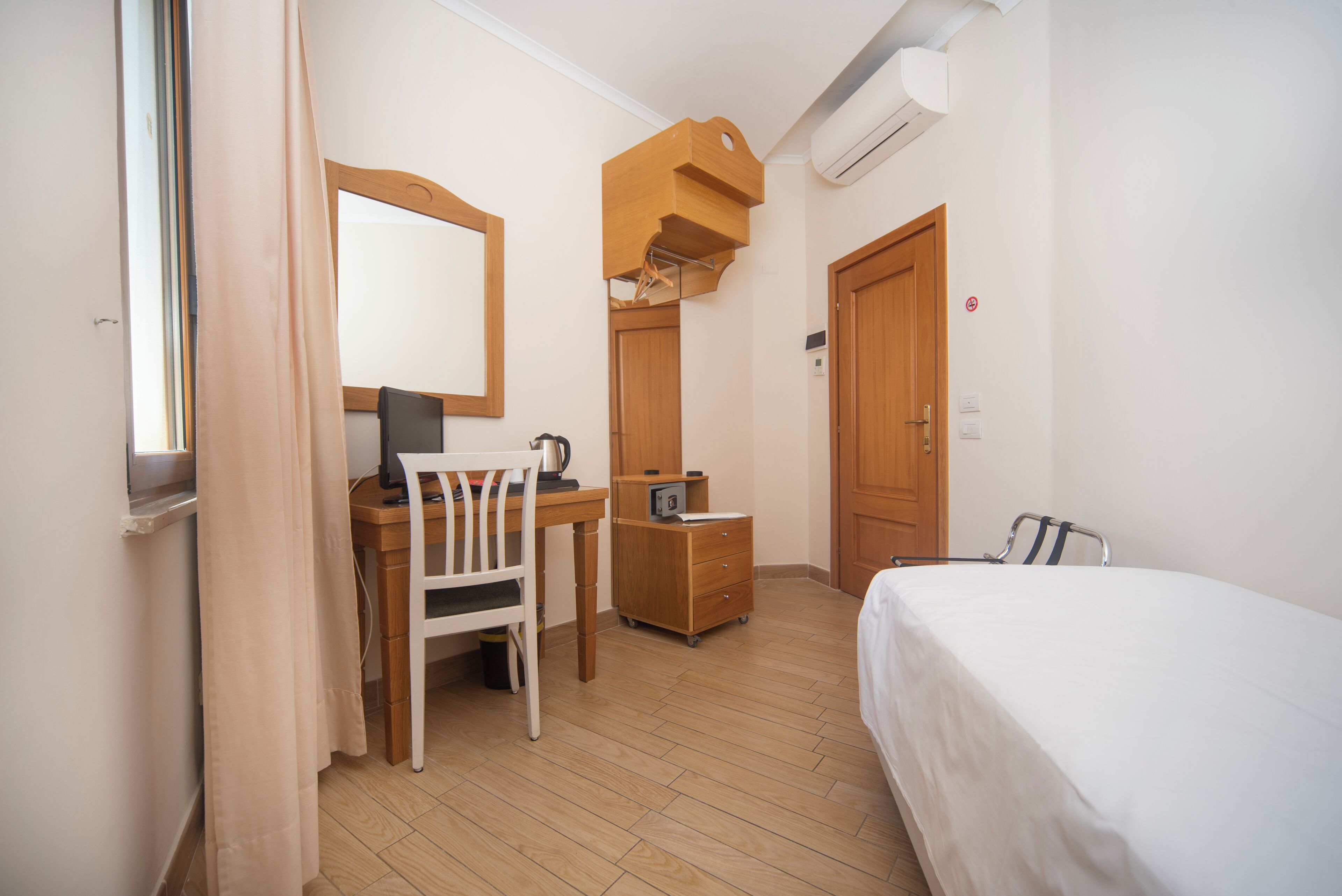 Une chambre d’hôtel avec un bureau en bois, une chaise et un lit. Il y a un miroir au-dessus du bureau et une armoire avec un miroir.