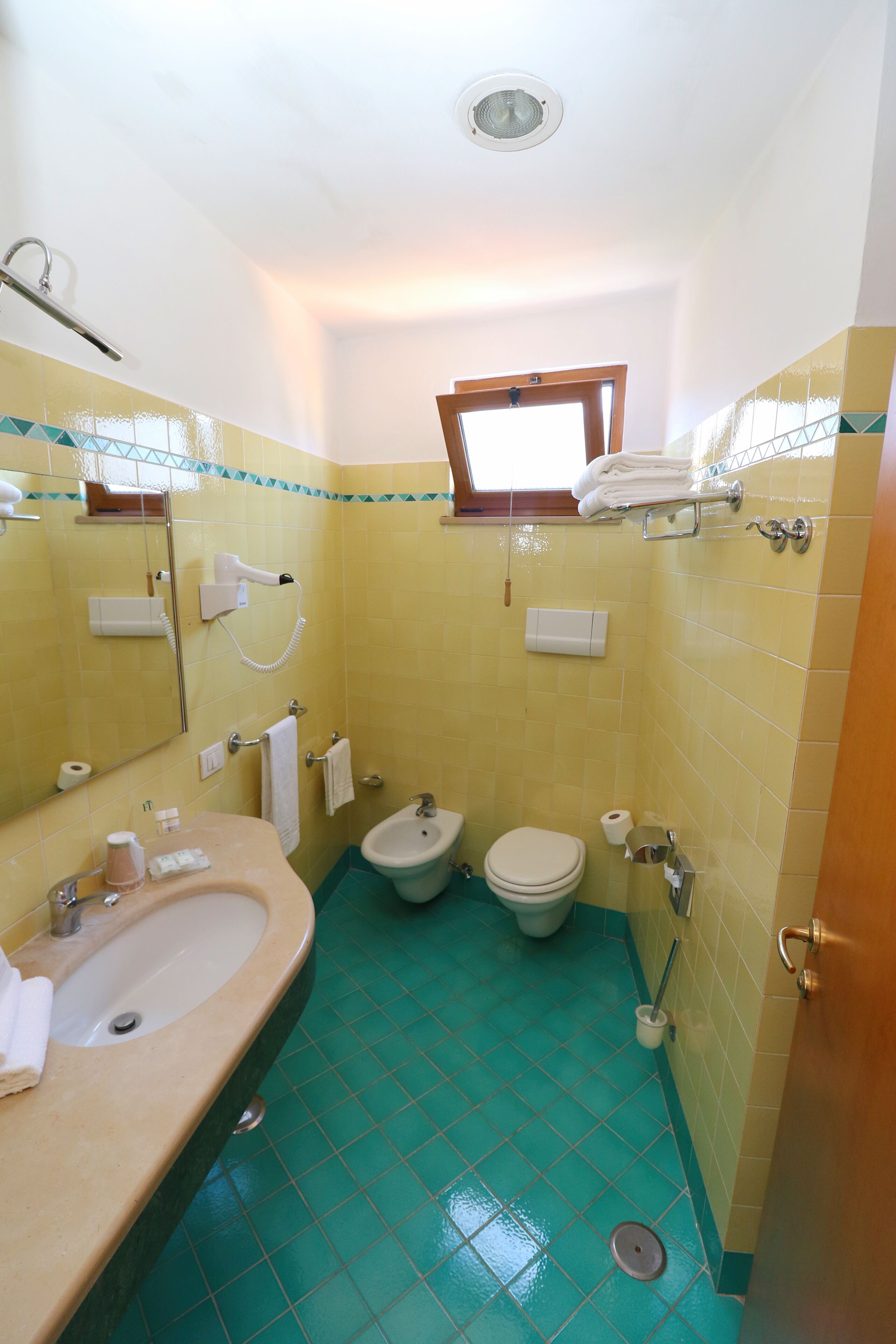 A bathroom with a sink, mirror, toilet, bidet, and a window.
