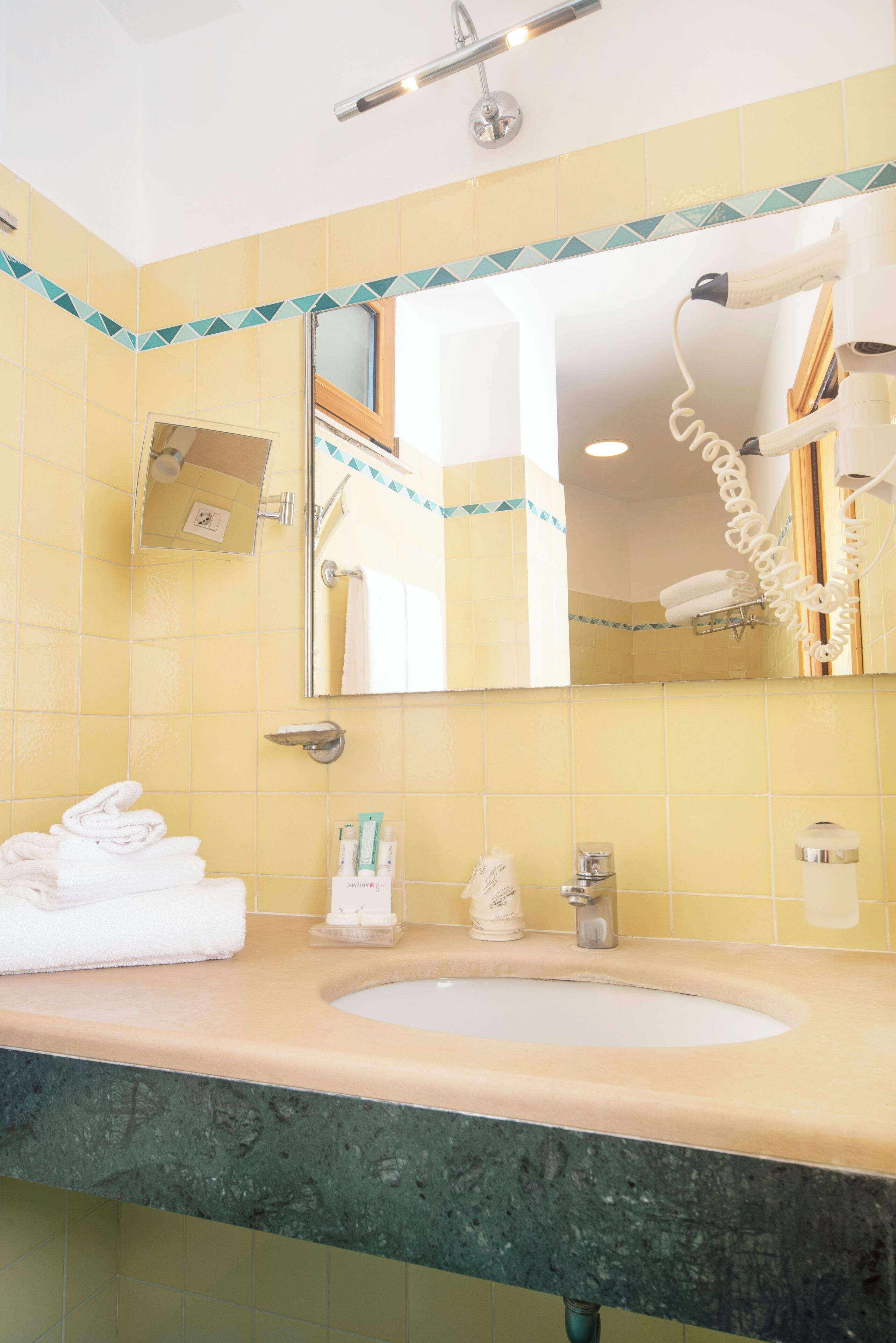 A bathroom with yellow tiles, a sink, a mirror, and a hairdryer.