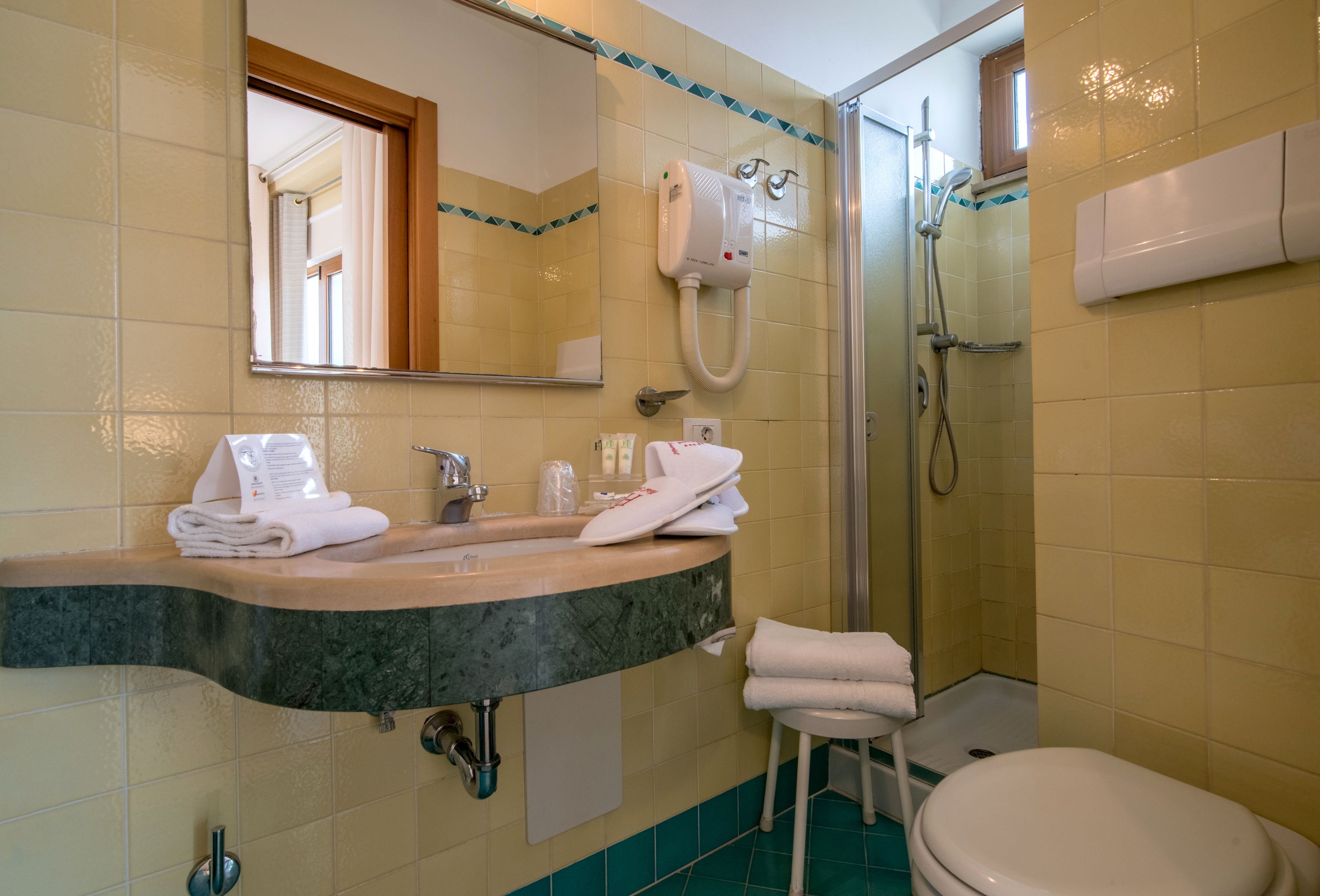 Bagno con lavandino, specchio, porta asciugamani, doccia e toilette.
