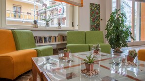 Una sala de estar con sofás verdes, una mesa de centro de vidrio con plantas de cactus y vistas a un balcón con flores y un letrero.