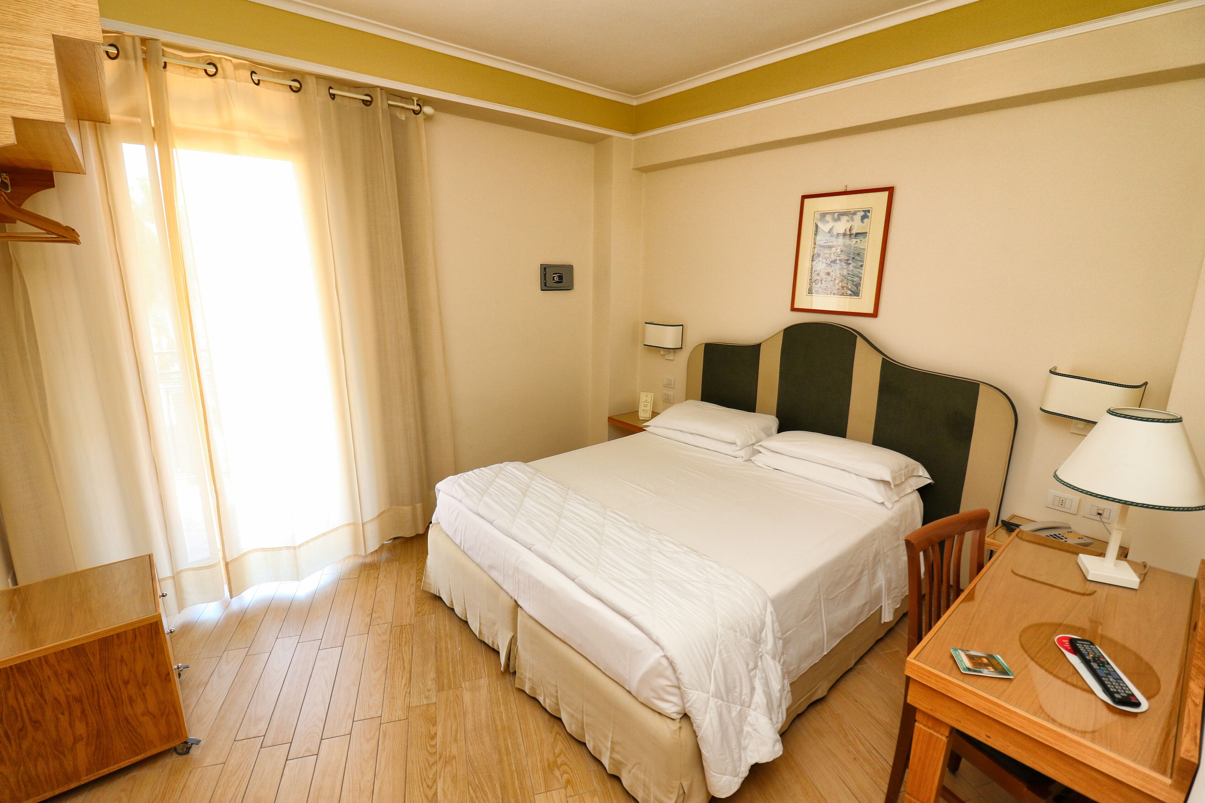 A hotel room with a bed, bedside table, lamp, and a desk with a chair.
