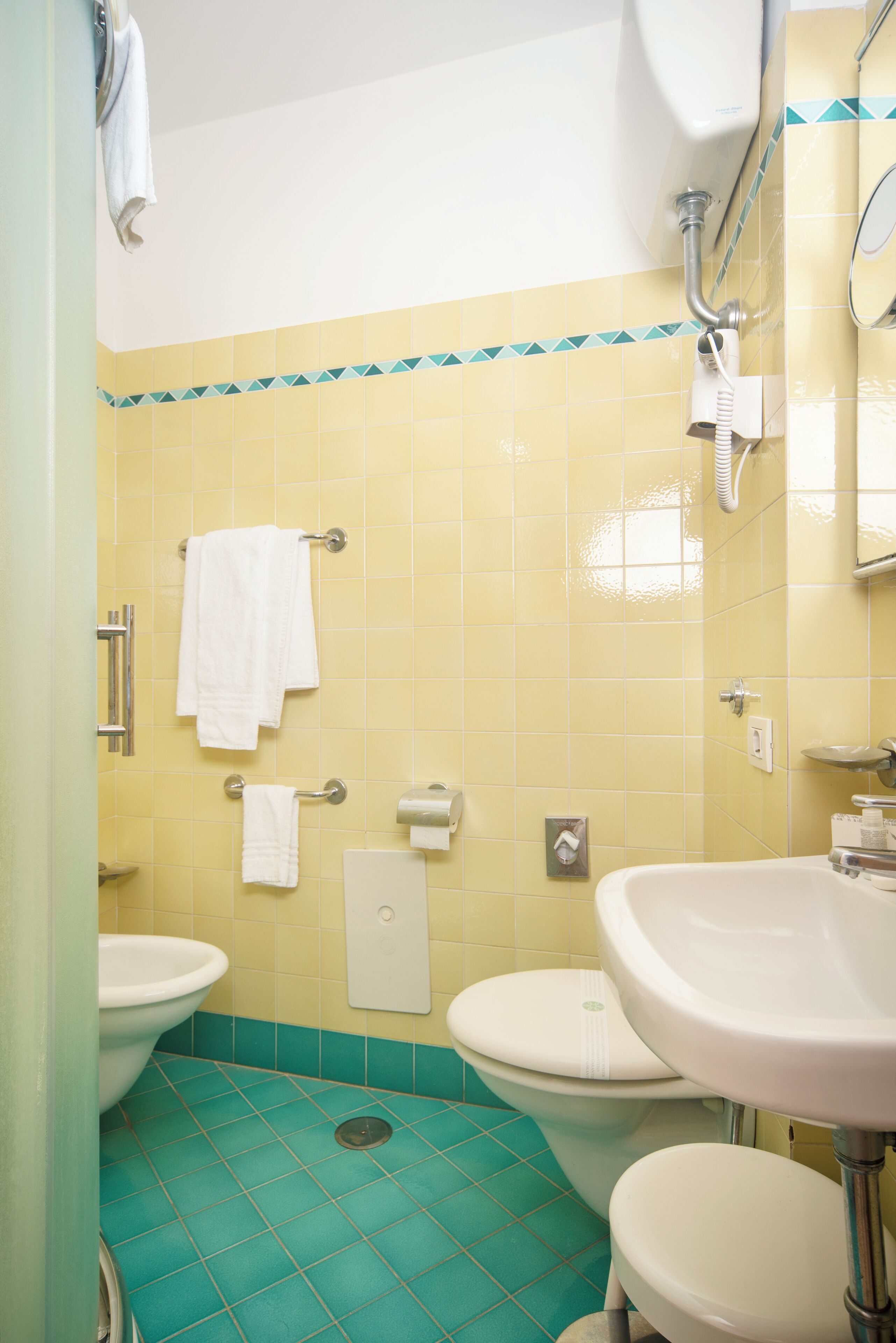 Ein Badezimmer mit gelben und türkisblauen Fliesen, einem weißen Waschbecken, einer Toilette und einer Dusche.