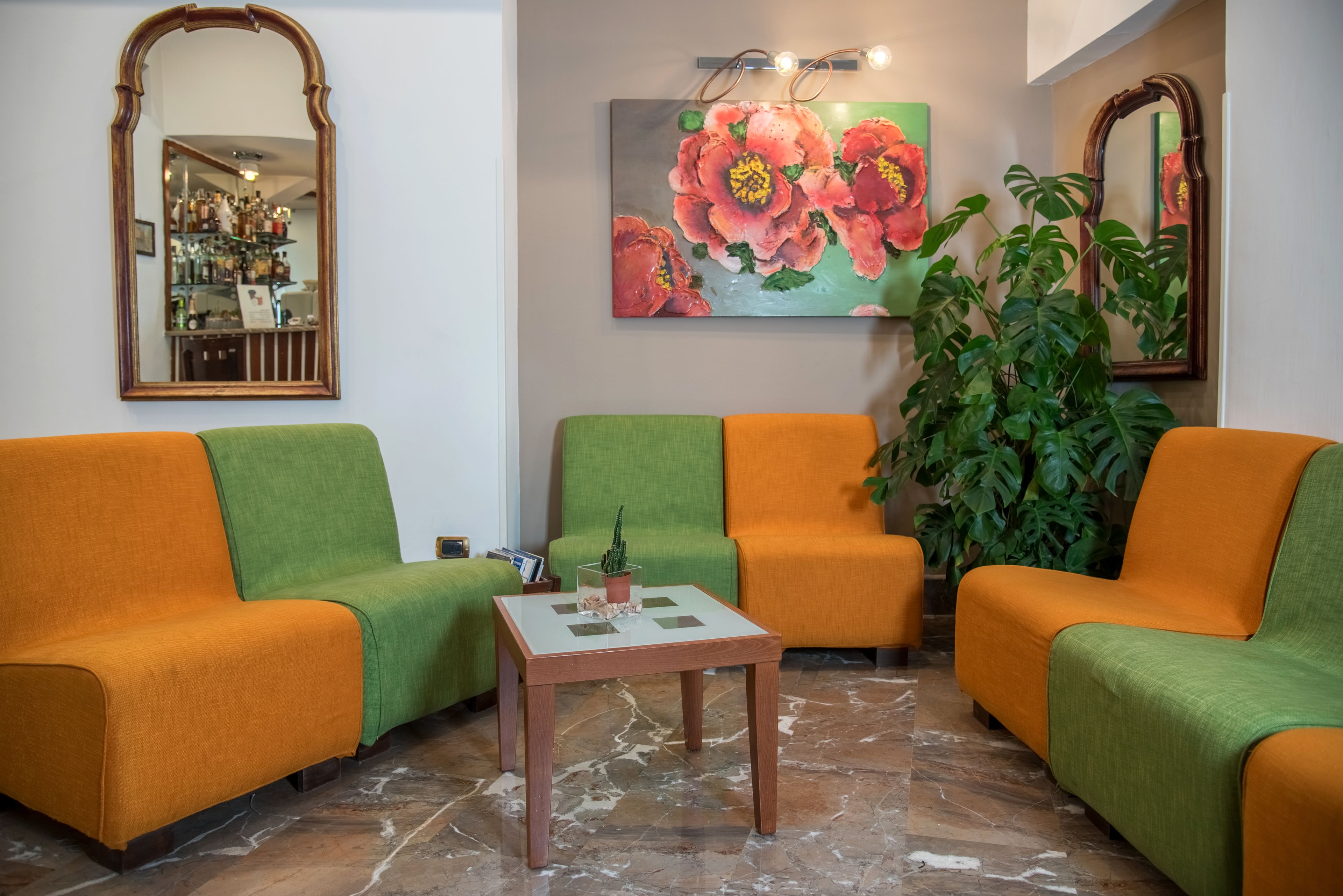 Un salon avec deux canapés verts et un canapé orange, une table basse et un tableau représentant des fleurs accroché au mur.