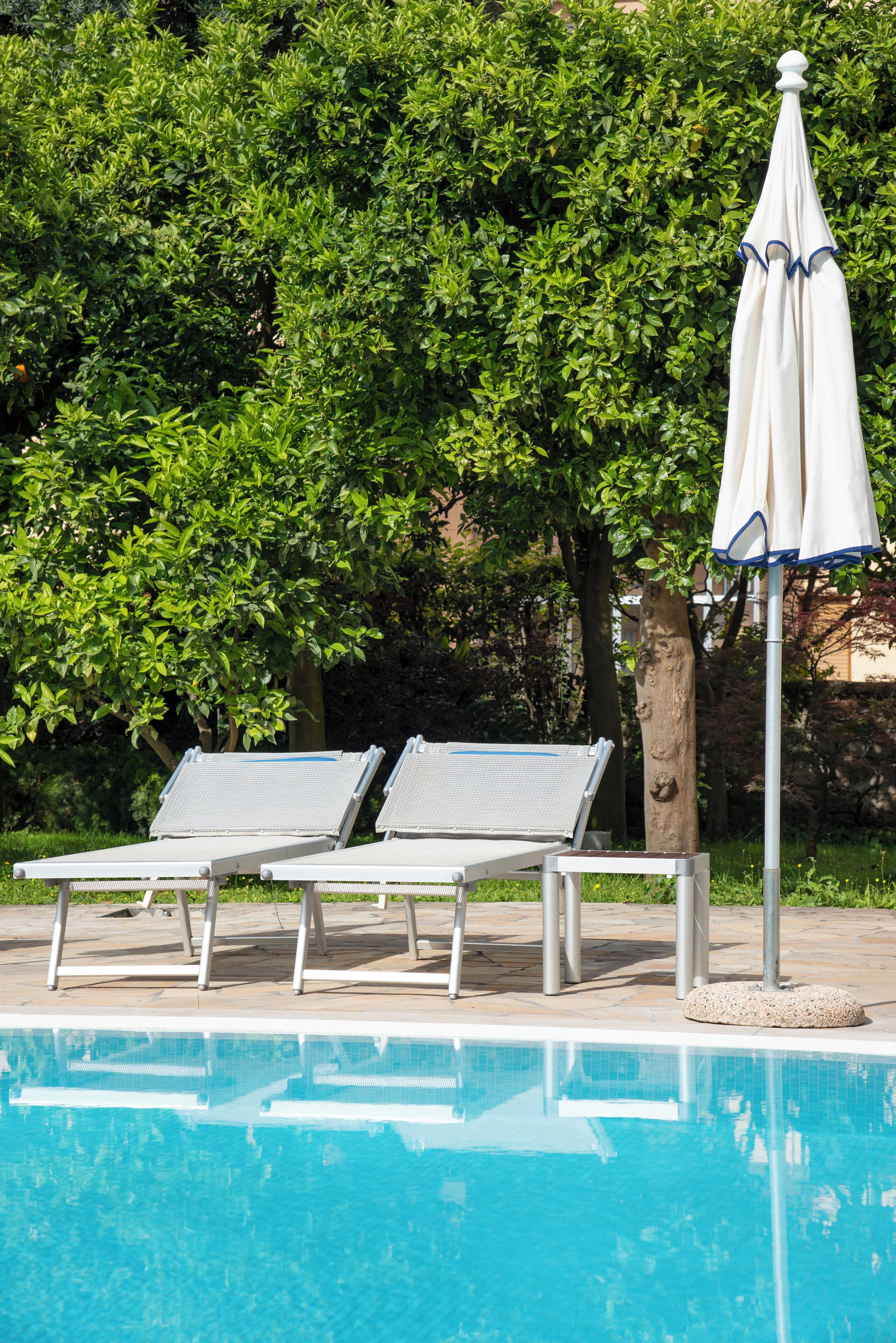 A swimming pool with two lounge chairs and a white umbrella.