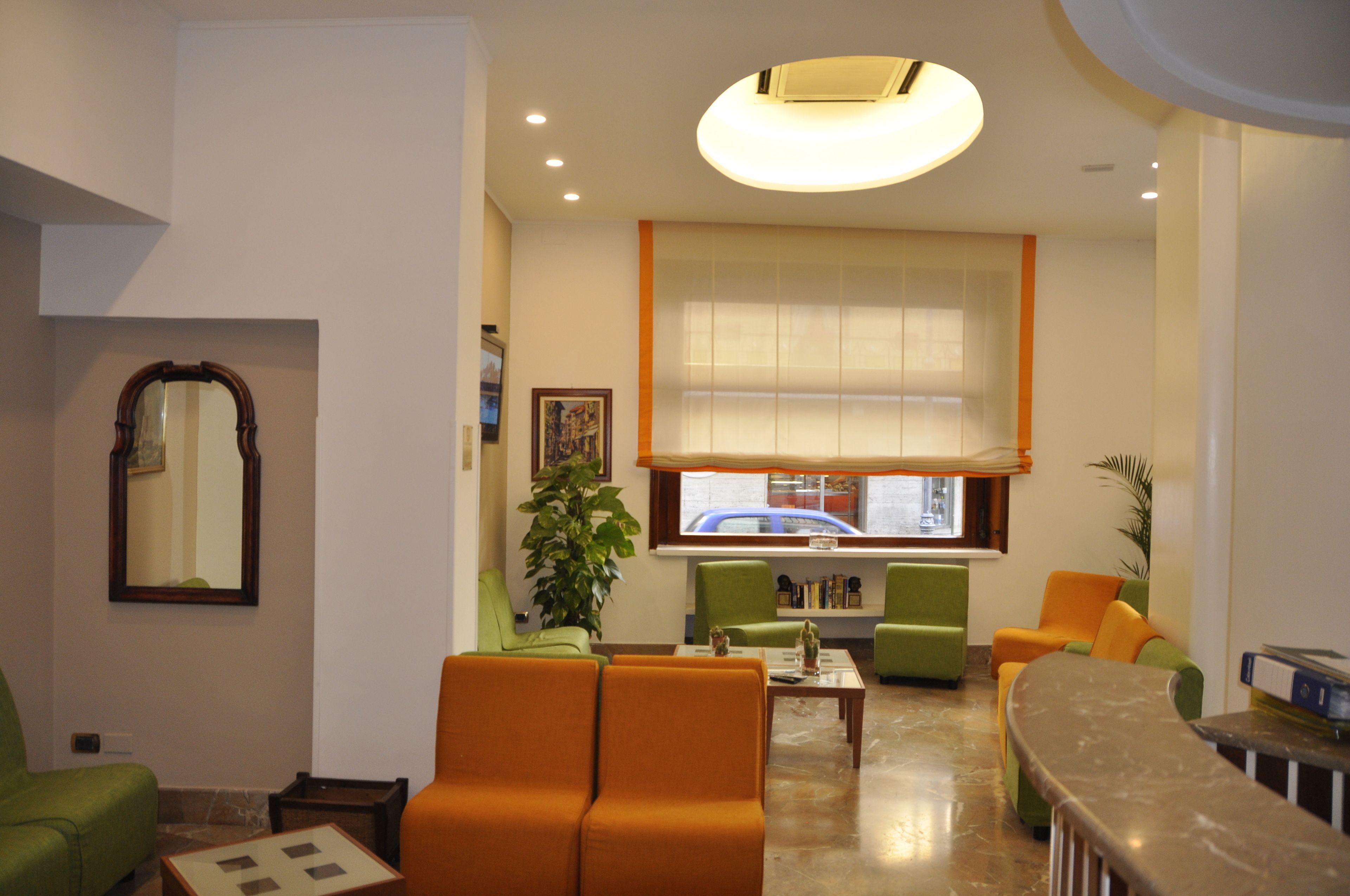 A modern living room with a large window, green and orange sofas, a coffee table, and a mirror on the wall.