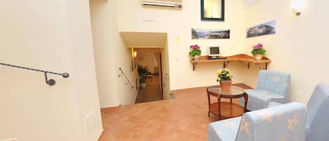 A living room with a sofa, a small table, and a TV. There is a staircase leading to another room.