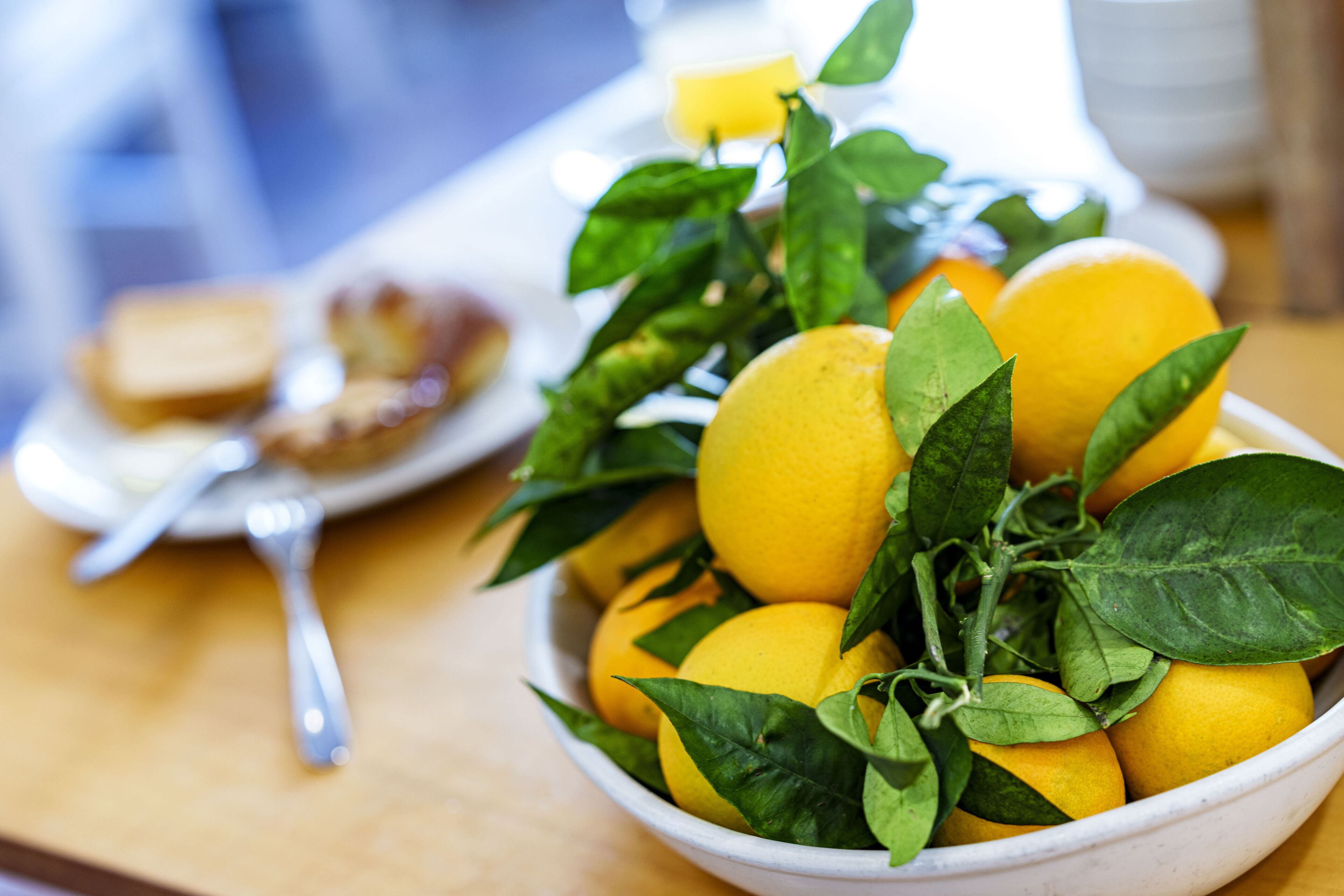 A bowl of lemons with leaves on a table.