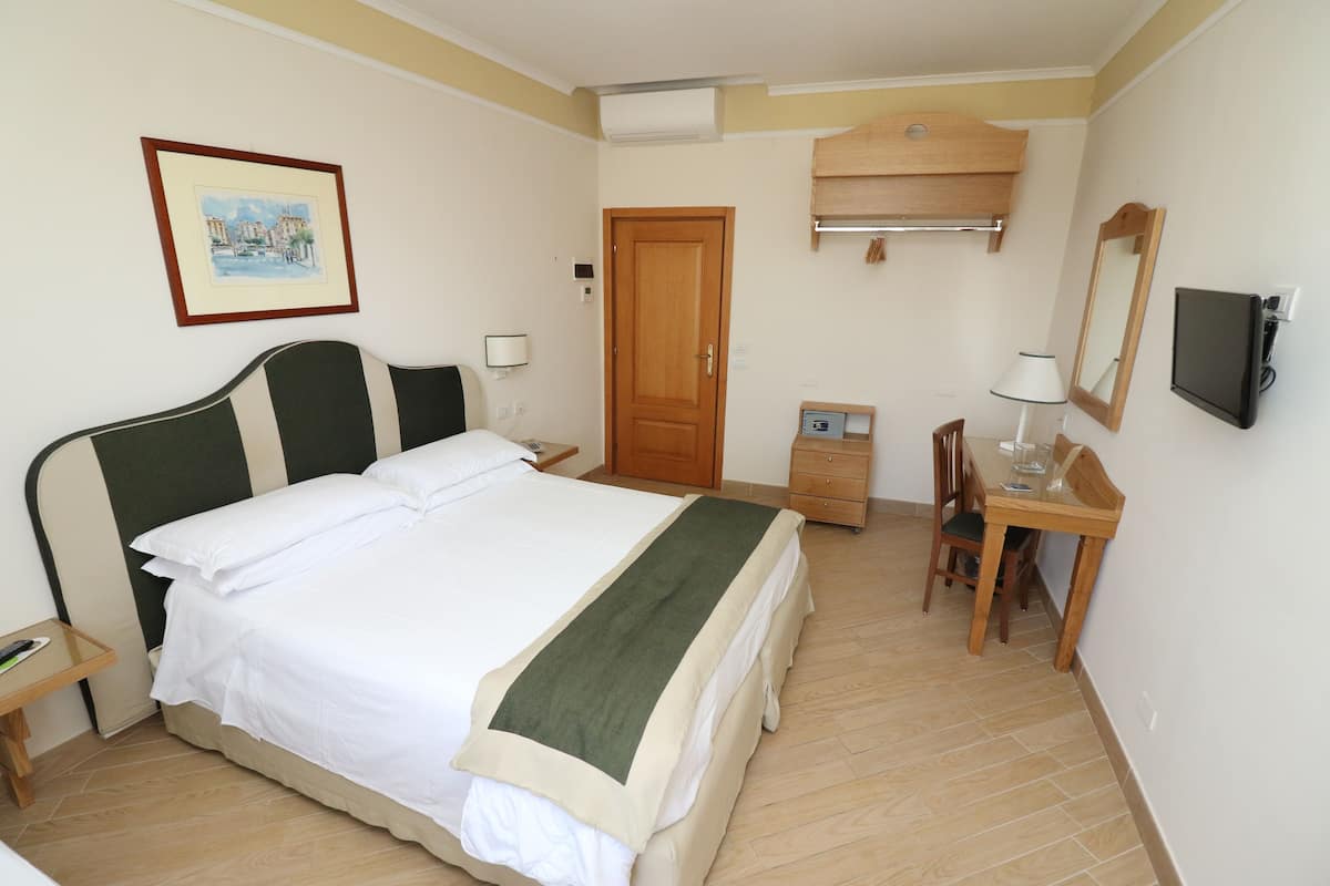 A hotel room with a bed, bedside table, desk, chair, and a television.