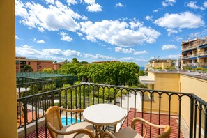 A balcony with a table and chairs, a pool, and a view of a cityscape with buildings and trees. - Hotel Capri - Adult Only (Sorrento)