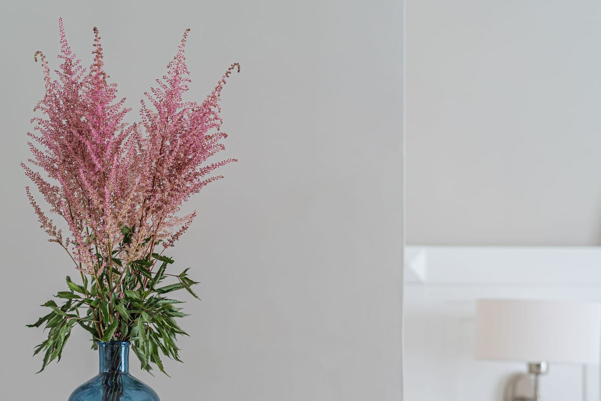 A white table with a blue vase containing pink flowers.