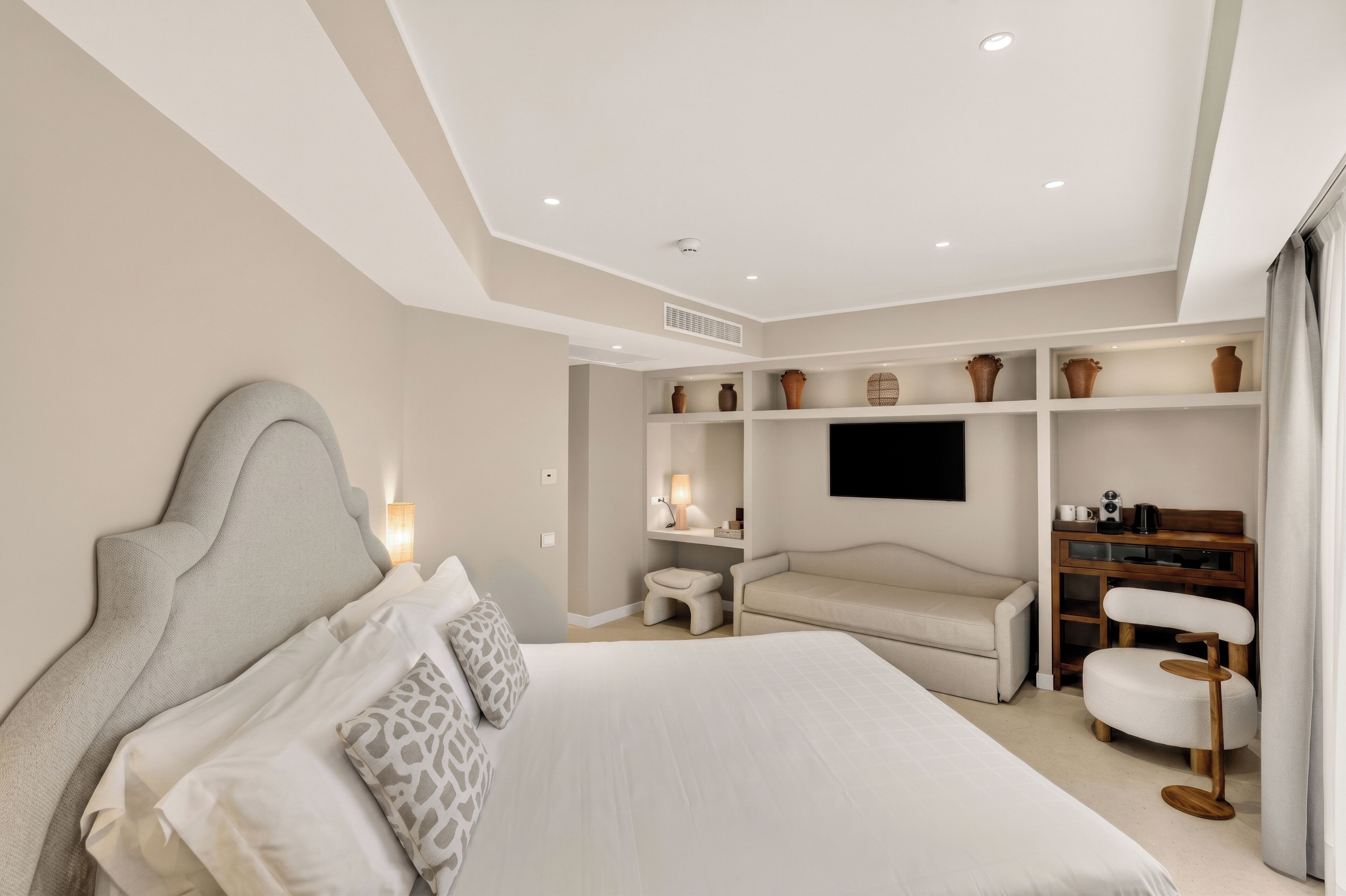 A modern bedroom with a large bed, a TV, and a seating area with a coffee table.