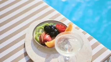 Un vassoio di frutta con un bicchiere e una bevanda su un tavolo a righe vicino a una piscina.