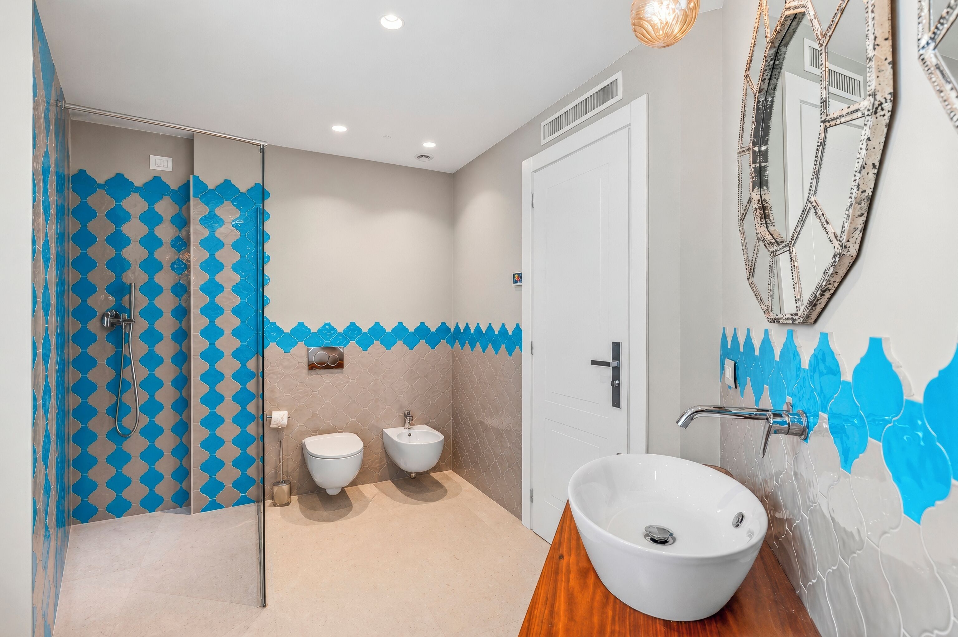 A bathroom with a glass shower enclosure, two bidets, a sink with a wooden vanity, and a mirror with a decorative frame.