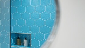 A bathroom with a blue hexagonal tile wall and a small shelf with toiletries. - Hotel Capri - Adult Only (Sorrento)