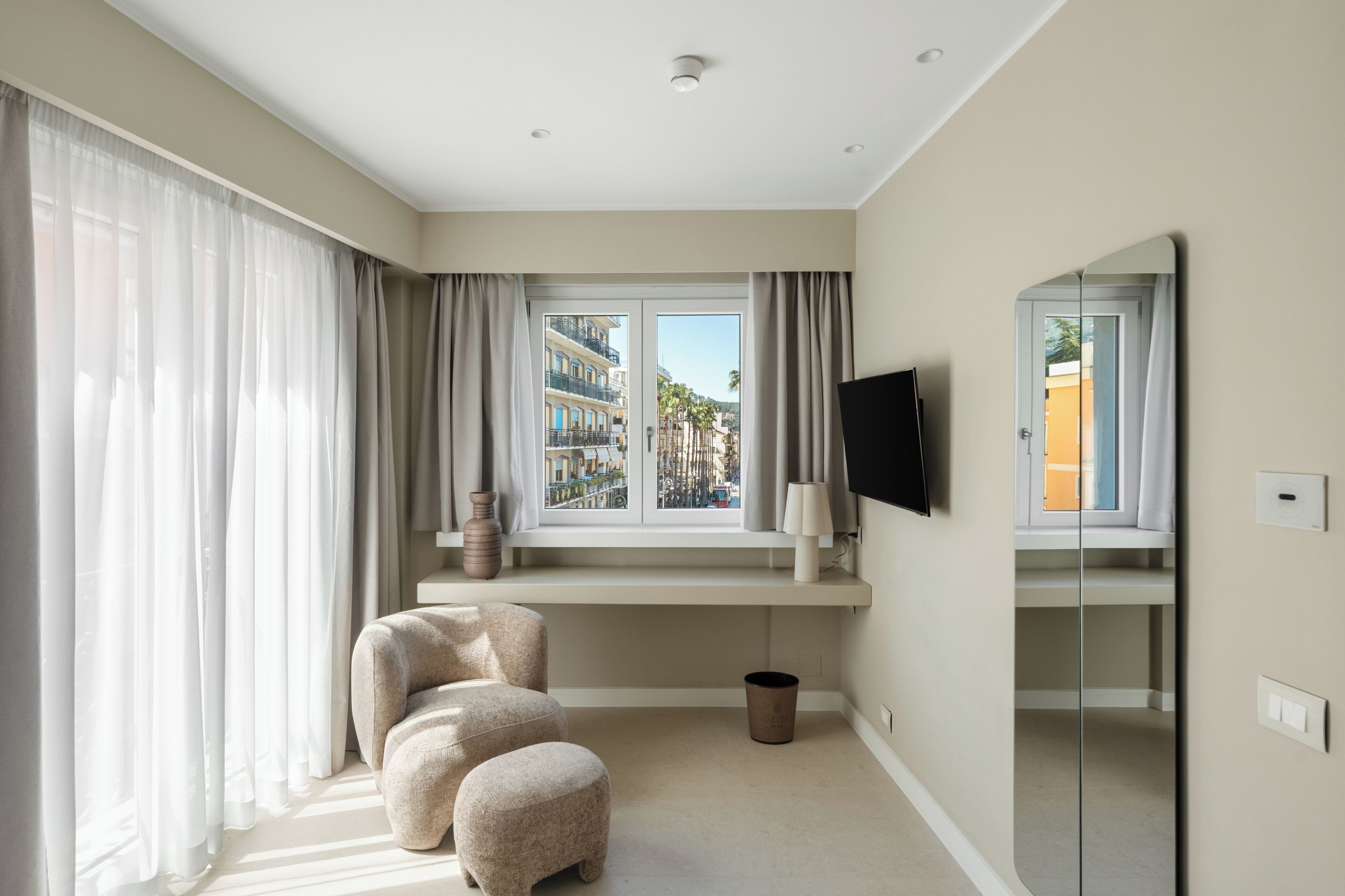 A hotel room with a large window, a sofa, a TV, and a mirror.