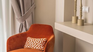 A corner room with a velvet orange armchair, a matching ottoman, and a white shelf with candles. - Hotel Capri - Adult Only (Sorrento)