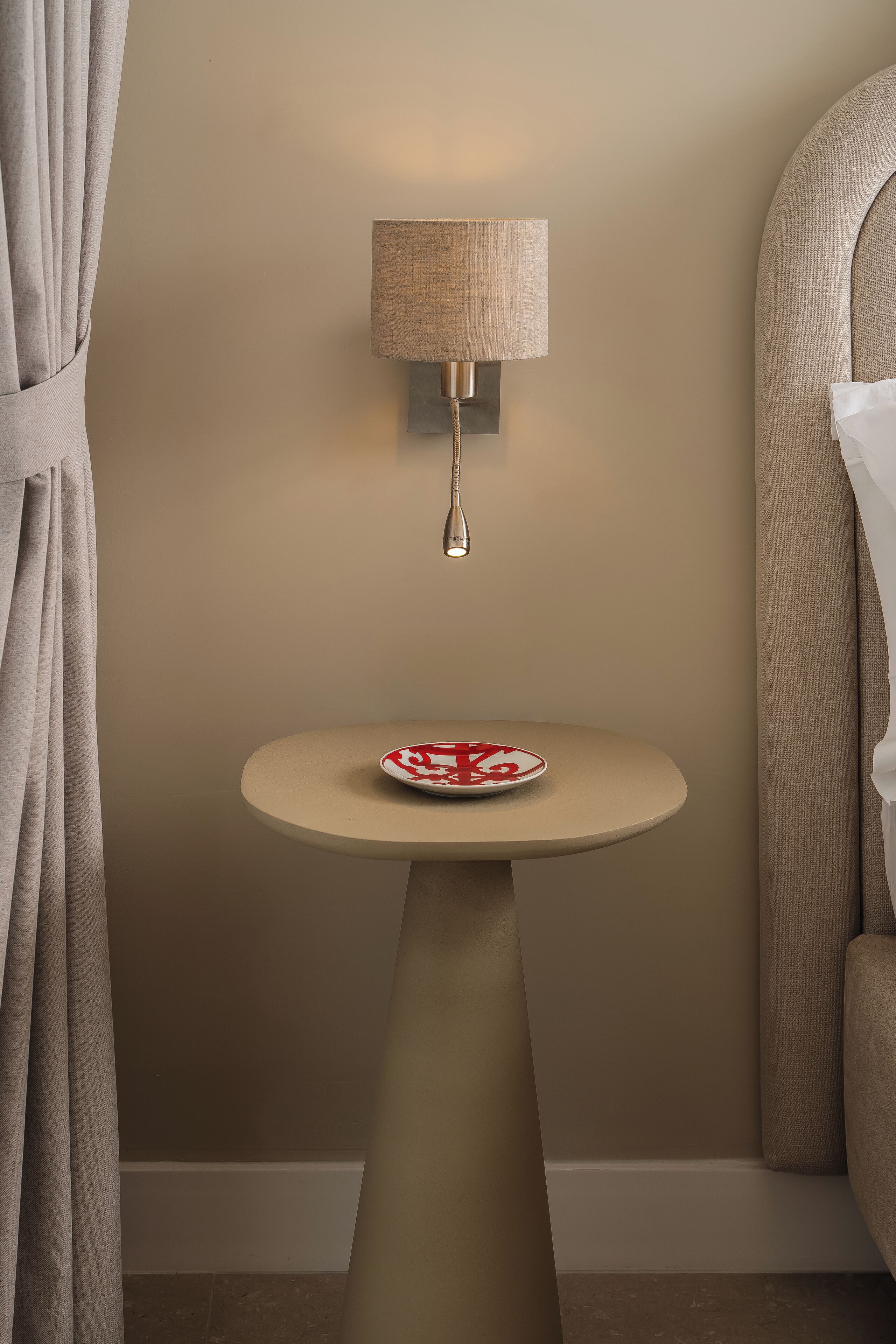 Una habitación con una mesa redonda, una lámpara de pared y una cortina.