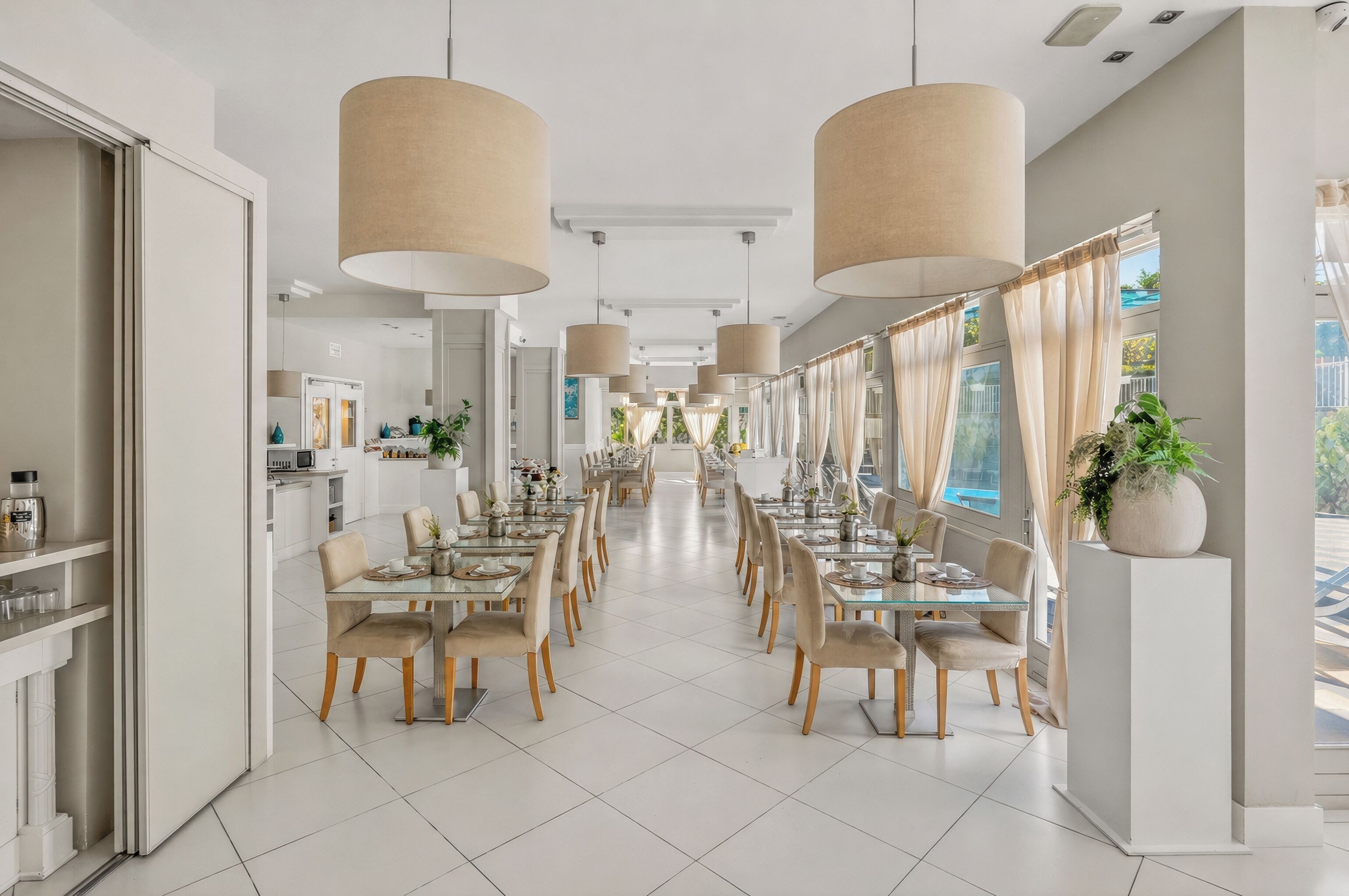 Un comedor moderno con mesas largas, sillas color beige y grandes lámparas colgantes.