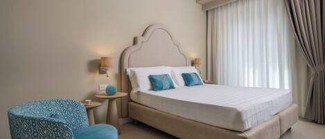 A bedroom with a large bed, a round blue chair, two bedside tables with lamps, and a window with curtains.